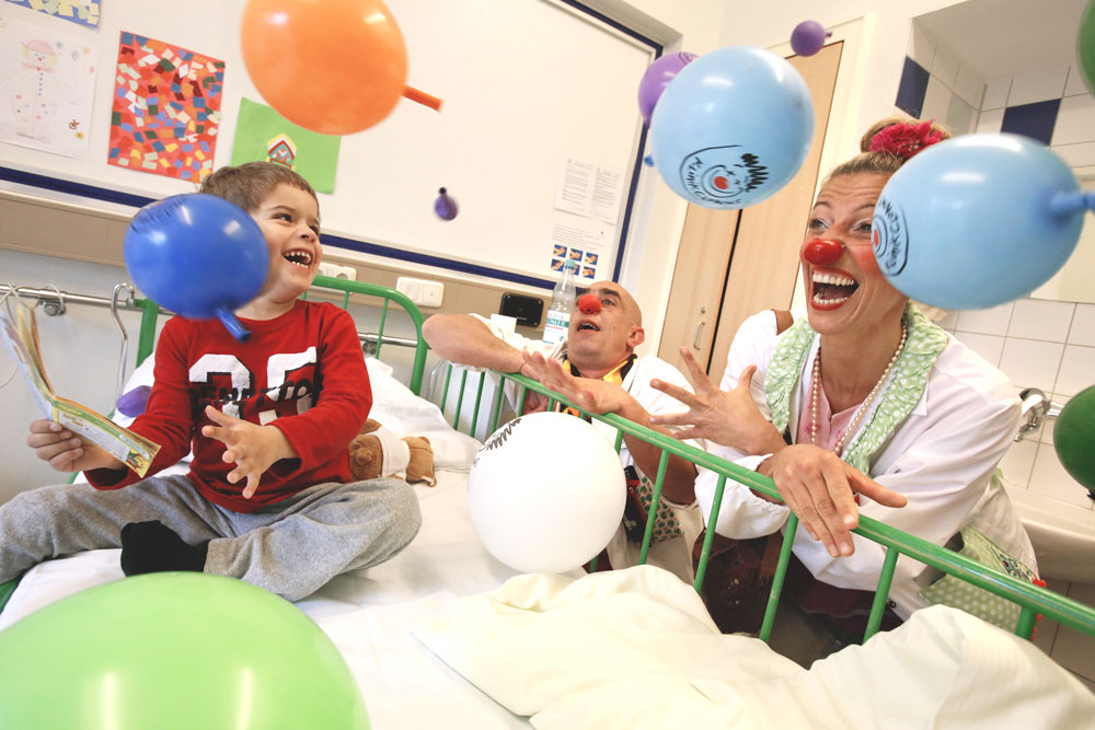Klinikclowns heitern einen Jungen im Krankenhaus mit Luftballons auf