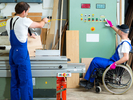 Zwei Arbeiter arbeiten in einer Werkstatt, einer der beiden sitzt im Rollstuhl